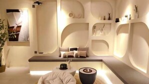 A modern, minimalist room with a sofa, a bean bag, and a round table. There are shelves with decorative items and a framed picture on the wall. - Jiuqi · Youran Seaside Holiday Apartment (Sanya)