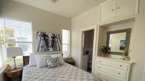 Un dormitorio con cama, mesita de noche, cómoda, espejo y un cuadro en la pared.