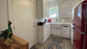 Una cocina compacta con armarios blancos, un refrigerador rojo y un pavo real decorativo sobre una mesa de madera.