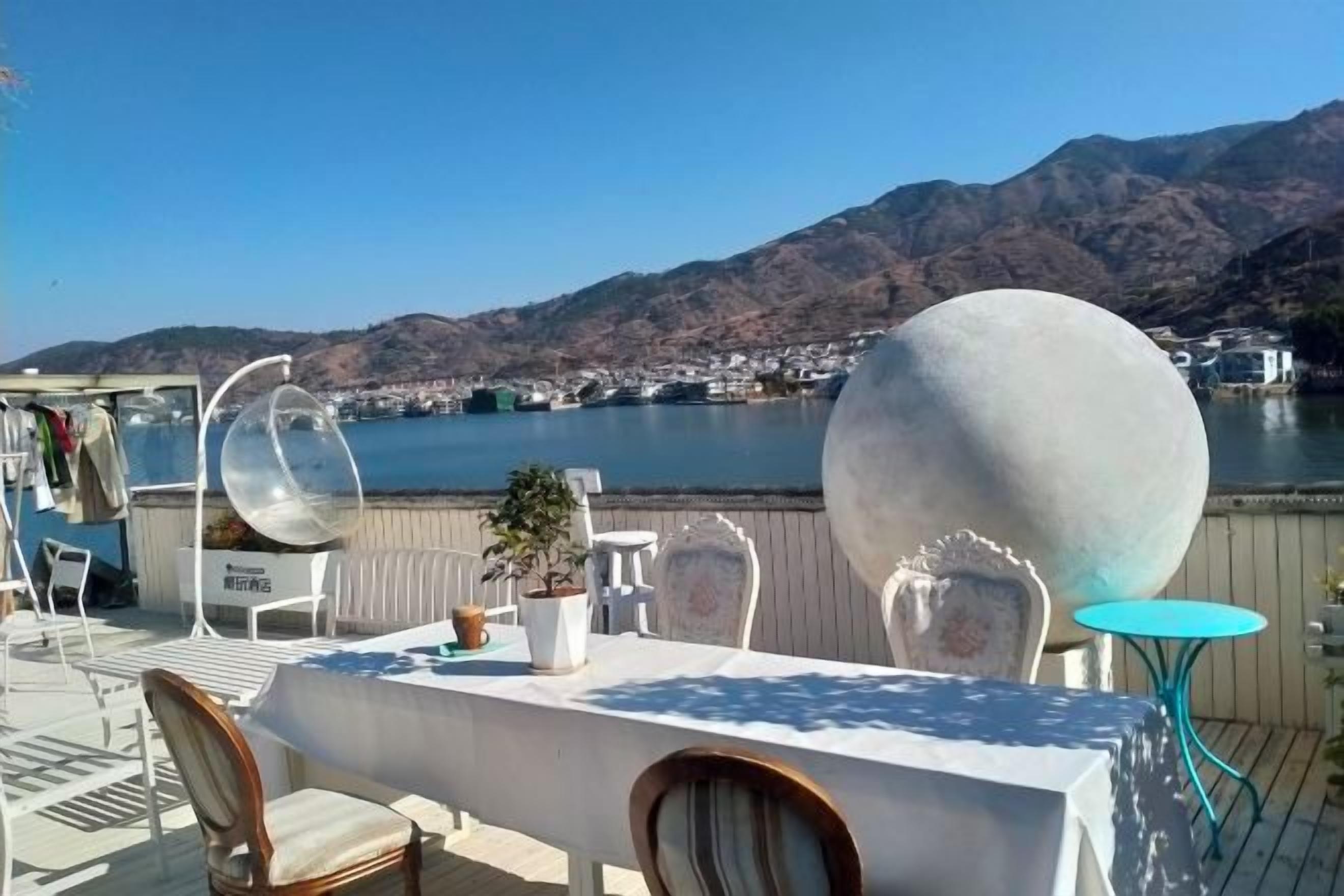 Un área de comedor al aire libre con una mesa y sillas, una planta en maceta y vistas a un lago y montañas.