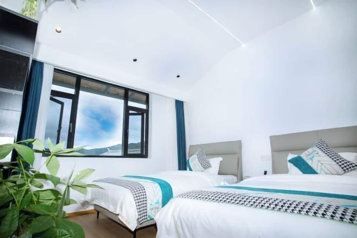 Ett modernt hotellrum med två sängar, ett stort fönster och en växt.