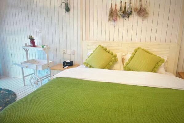 A bedroom with a bed, green pillows, a small table with a lamp, and a wall-mounted shelf with decorative items. - Dali Old Time Seaview Inn (Dali City)
