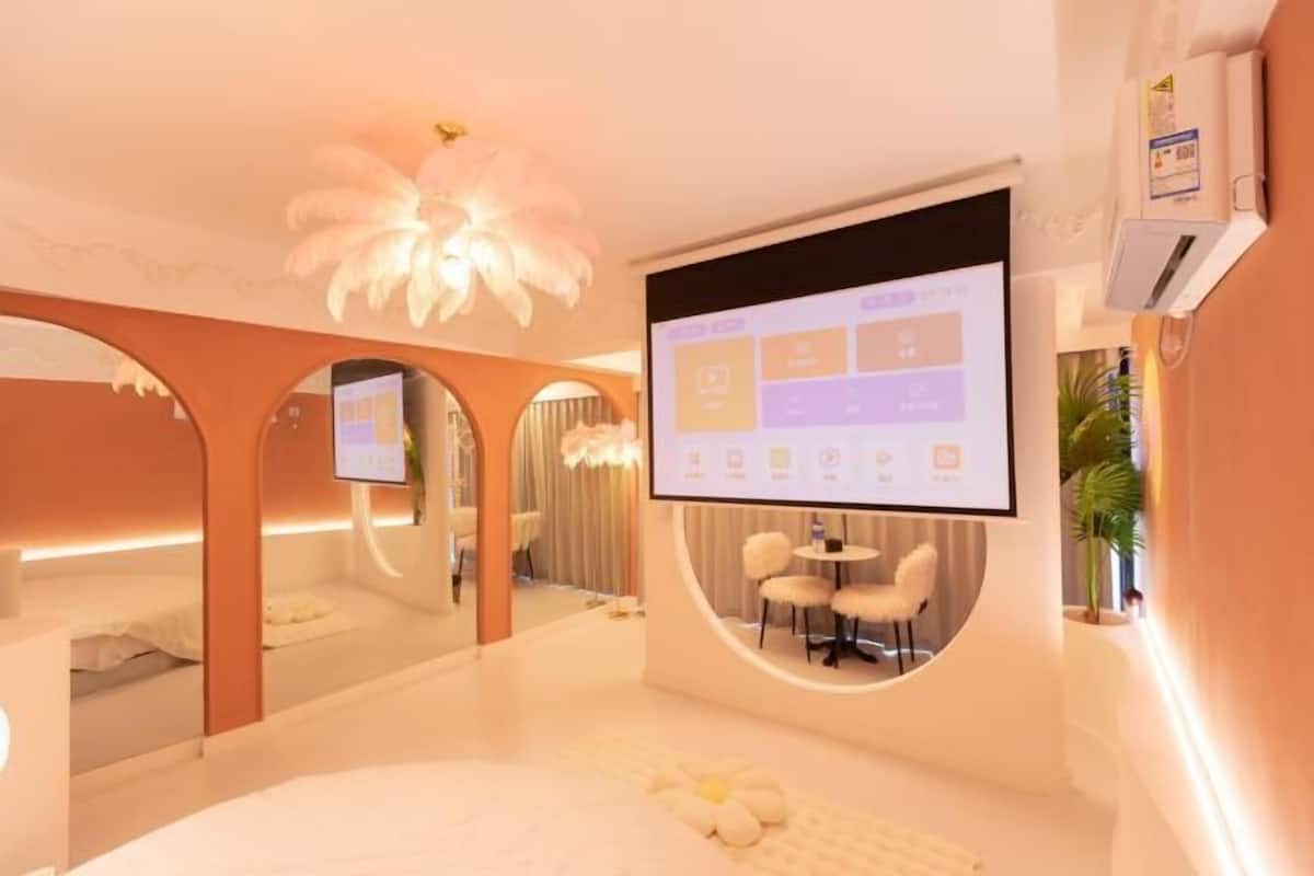 Ett modernt hotellrum med en stor säng, en tv-skärm, ett litet bord och en spegel.