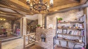 A cozy interior with a brick fireplace, wooden beams, and a bookshelf with various items.