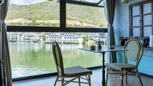 A room with a table and two chairs, a window with a view of boats and hills, and a sign reading 'Coffee'.