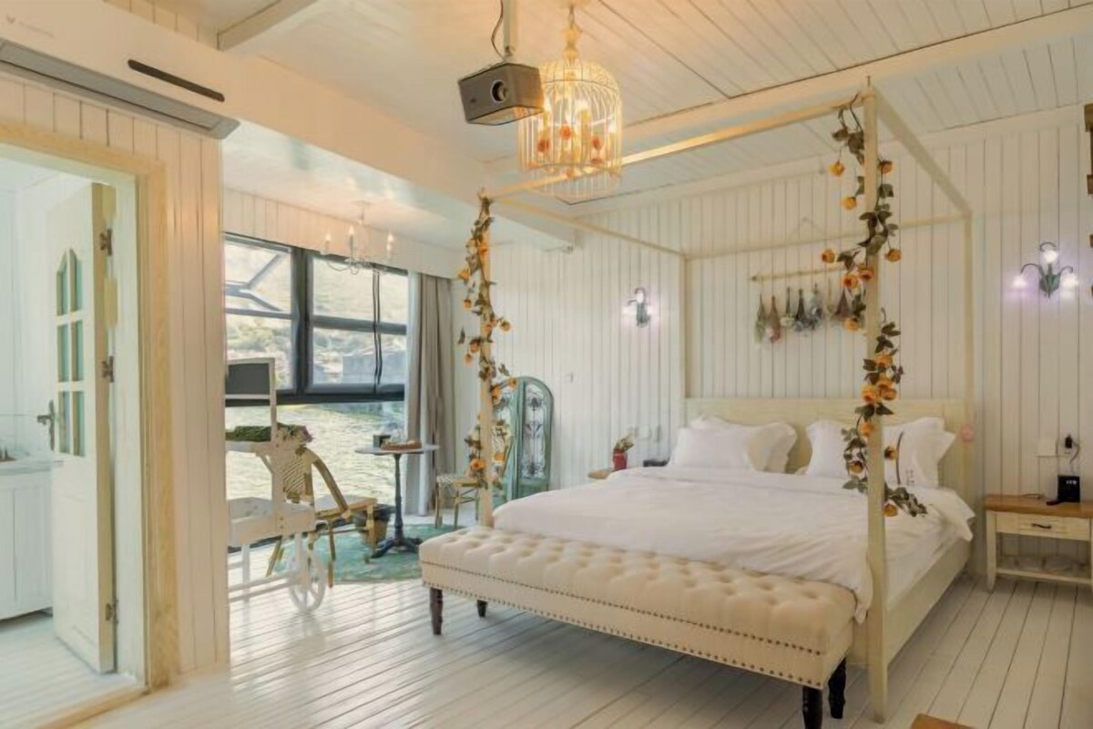 A bedroom with a four-poster bed, a chandelier, and a view of the outdoors.