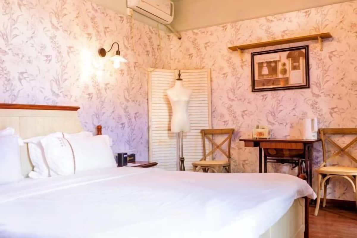 Ett hotellrum med en säng, ett skrivbord, två stolar, en lampa och en inramad tavla på väggen.