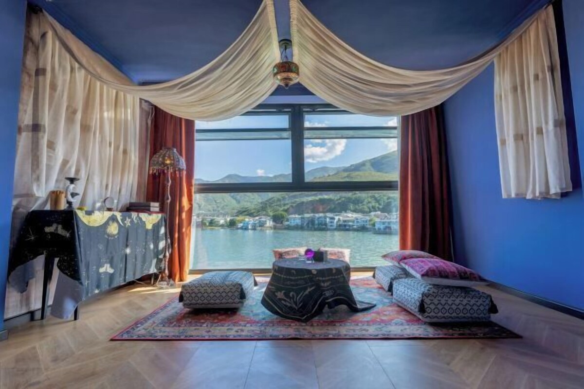 A room with a large window, a bed, a table, and a chair.