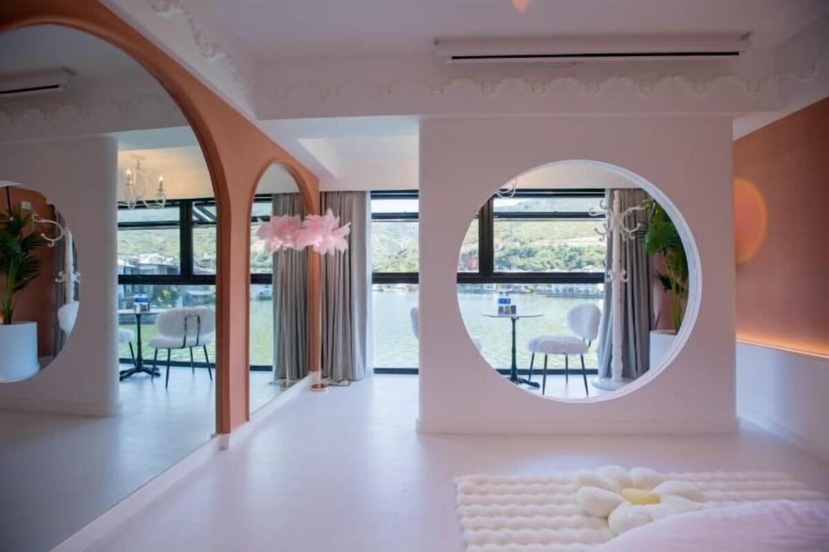 A modern hotel room with a large bed, a circular window, and a view of the outdoors.