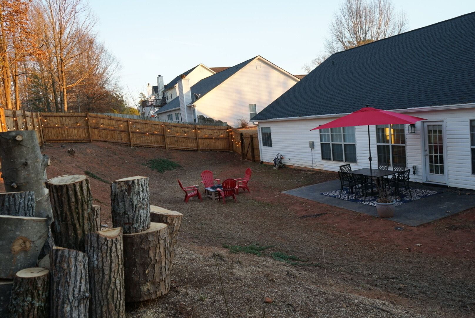 A backyard with a patio area, red Adirondack chairs, and a red umbrella.