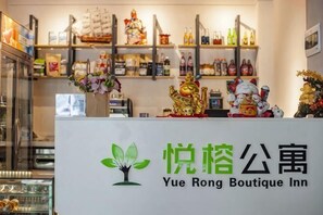 Een hotel receptiebalie met een bord waarop 'Yue Rong Boutique Inn' staat, planken met verschillende spullen en een decoratief beeld.