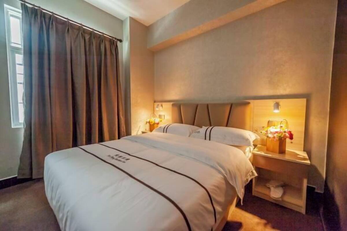 Une chambre d’hôtel avec un grand lit, une table de chevet avec une lampe et une fenêtre avec des rideaux.