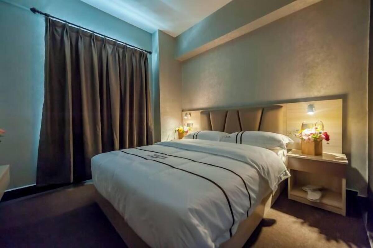 Une chambre d’hôtel avec un grand lit, une table de chevet avec une lampe et une fenêtre avec des rideaux.