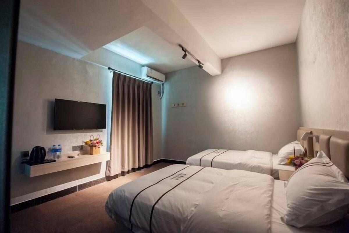 Une chambre d’hôtel avec deux lits, une télévision, une étagère avec des articles de toilette et une fenêtre avec des rideaux.