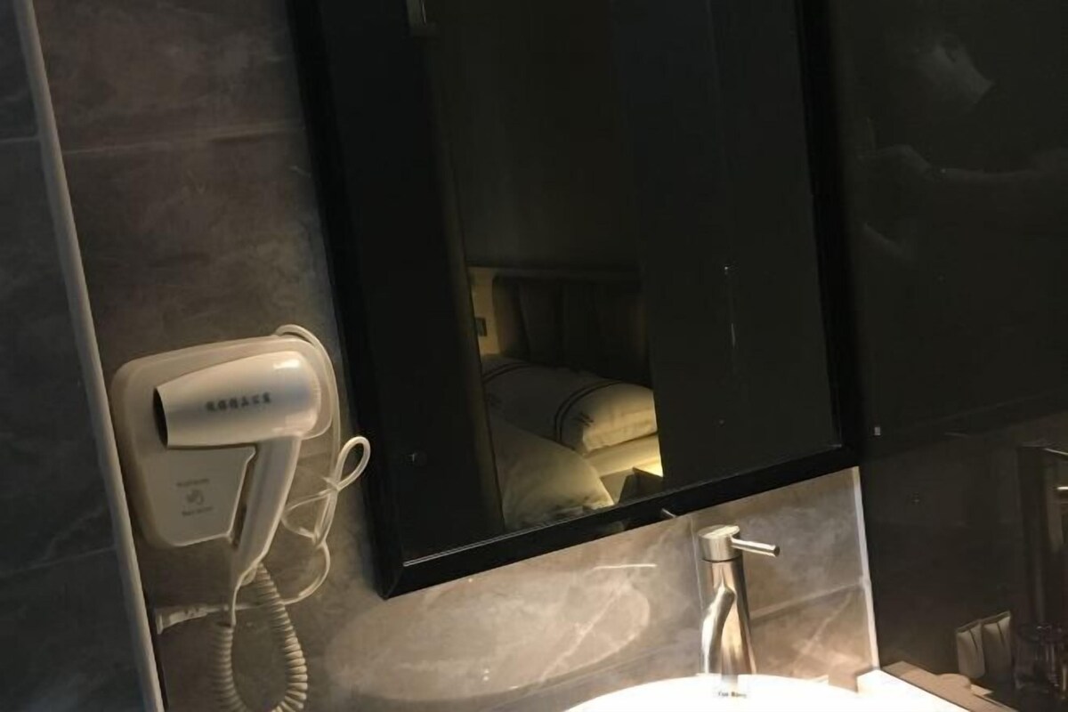 A hotel room with a hairdryer, a mirror, and a sink.
