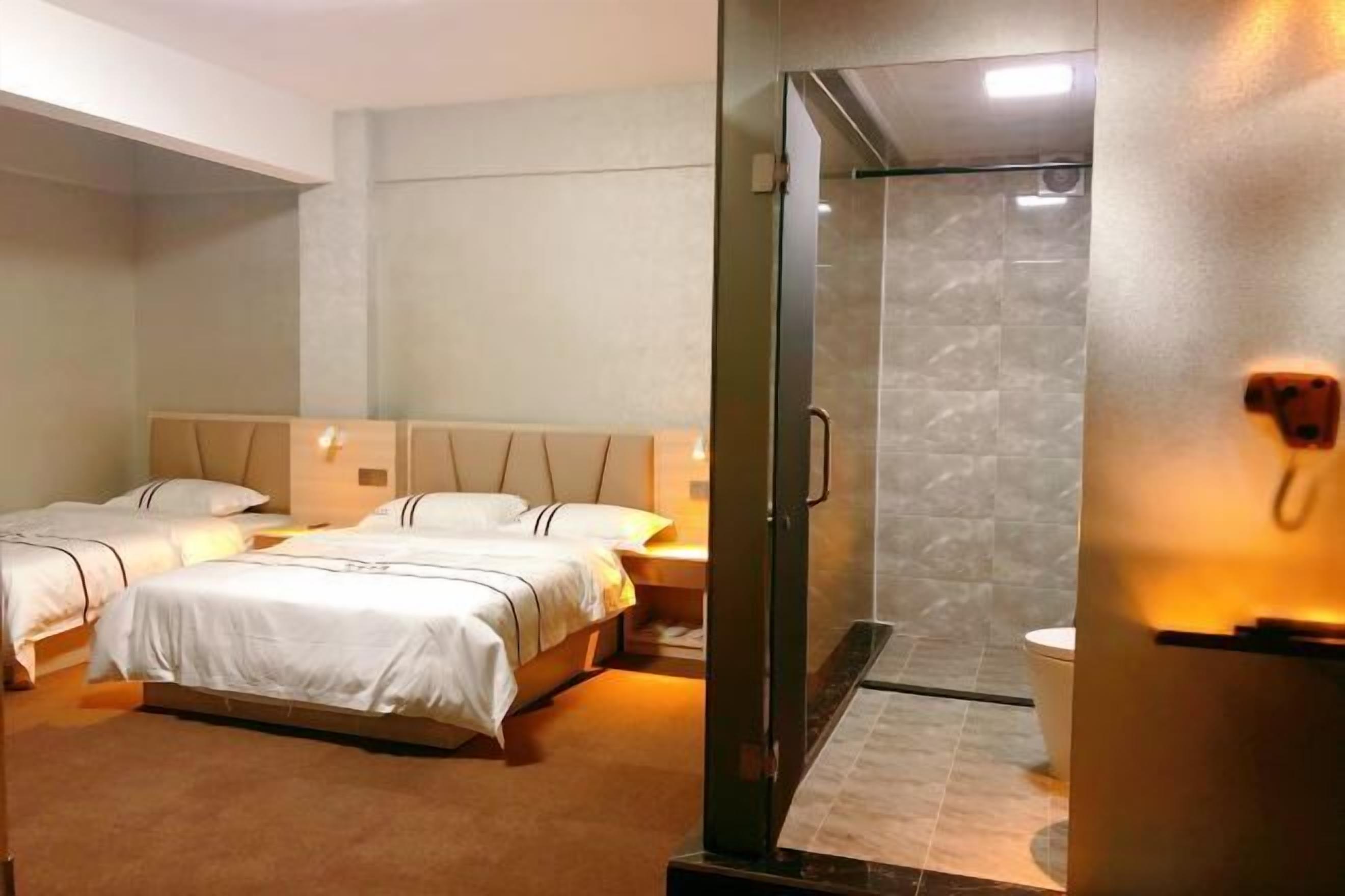 Habitación de hotel con dos camas, cabina de ducha de vidrio y baño a la vista.