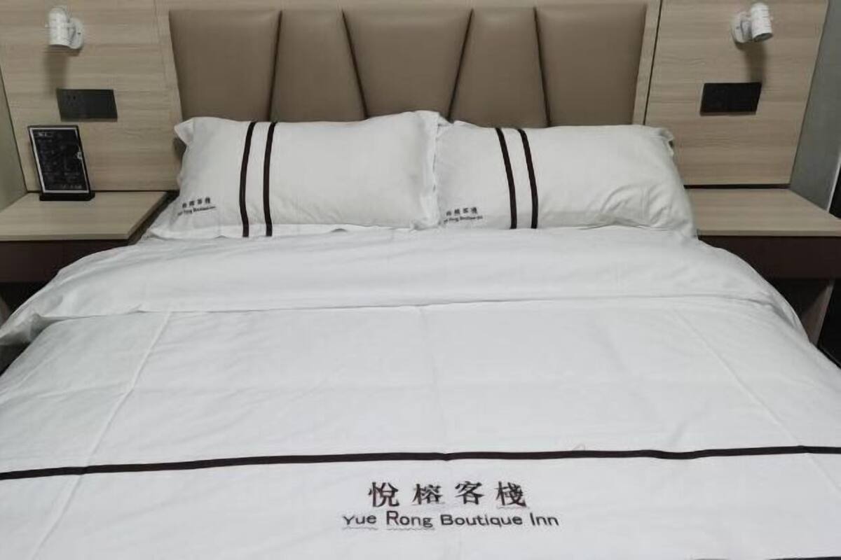 Un lit avec une literie blanche à rayures noires, une tête de lit et deux tables de chevet sur lesquelles sont posées des lampes et un petit appareil.