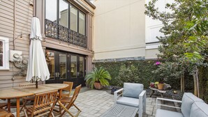 A patio with a wooden table and chairs, a white sofa, and a potted plant. - Your Beautiful Savannah House: Picturesque Inside and Out! Walk to Everything (Savannah)