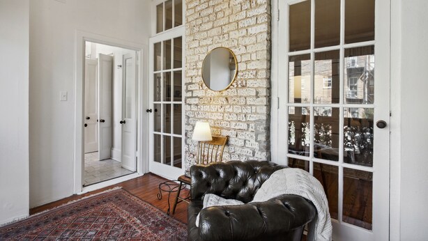 A room with a brick wall, a round mirror, a leather sofa, and a patterned rug. - Your Beautiful Savannah House: Picturesque Inside and Out! Walk to Everything (Savannah)