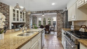 A kitchen with granite countertops, stainless steel appliances, and a brick wall. - Your Beautiful Savannah House: Picturesque Inside and Out! Walk to Everything (Savannah)