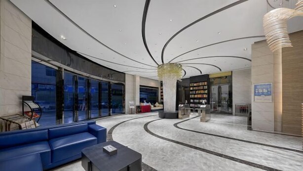 Um lobby moderno com área de estar em curva, uma coluna central e uma grande estante de livros.