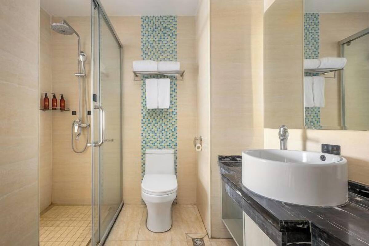 A modern bathroom with a glass shower enclosure, a white toilet, a sink with a marble countertop, and a tiled backsplash.