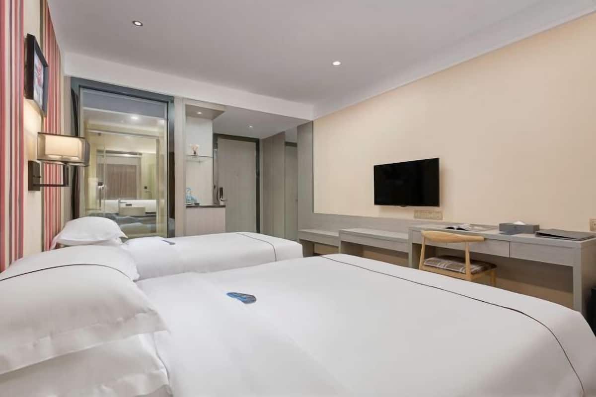 A hotel room with two beds, a desk, a chair, a TV, and a bathroom visible through an open door.