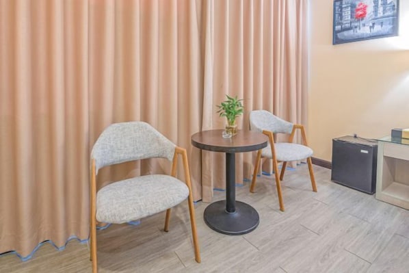 Um quarto com duas cadeiras, uma mesa redonda pequena, um vaso de planta e um armário pequeno.