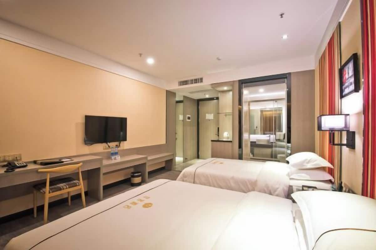 A hotel room with two beds, a desk, a chair, a TV, and a mirror.