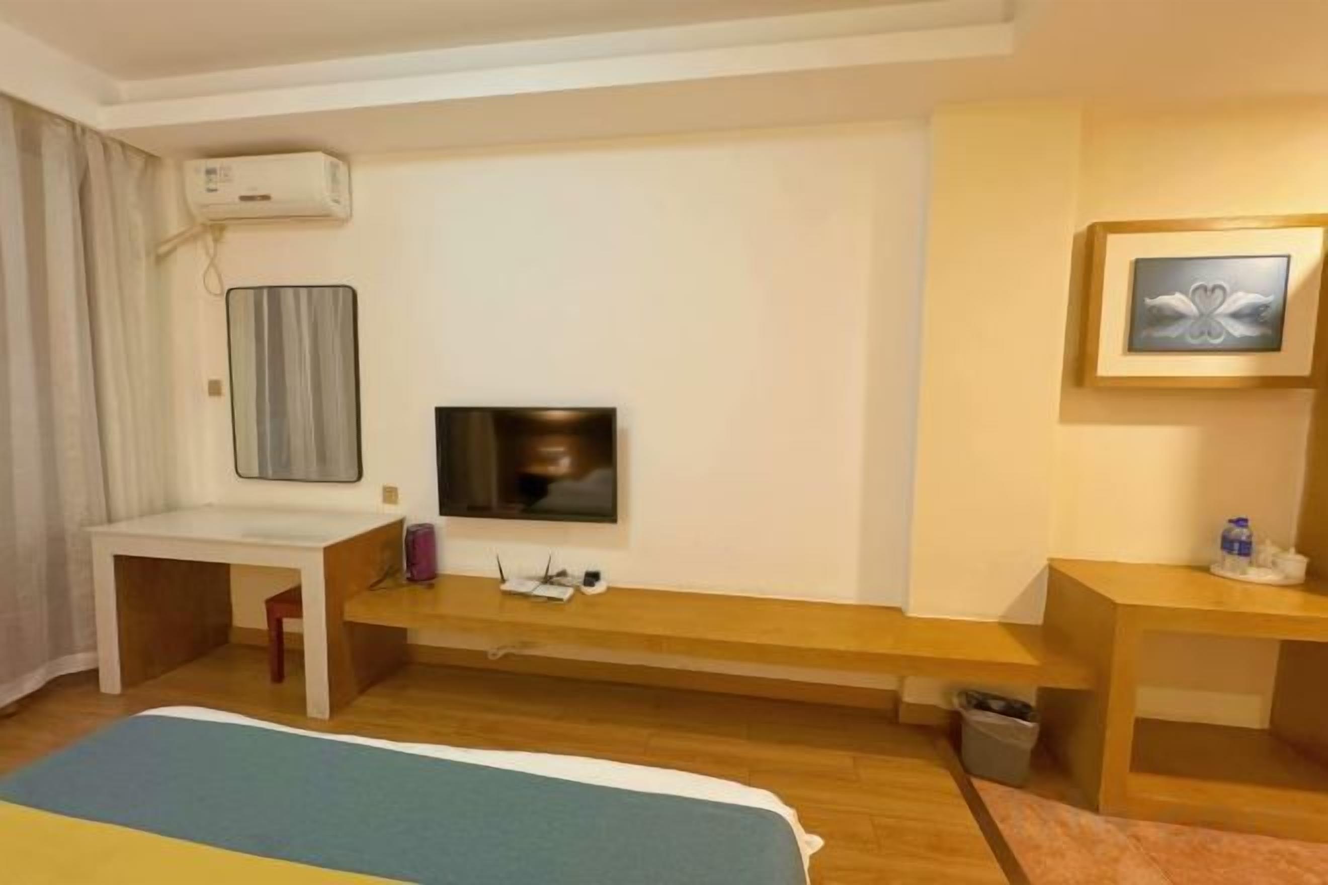 A hotel room with a bed, a desk, a TV, and a bench.