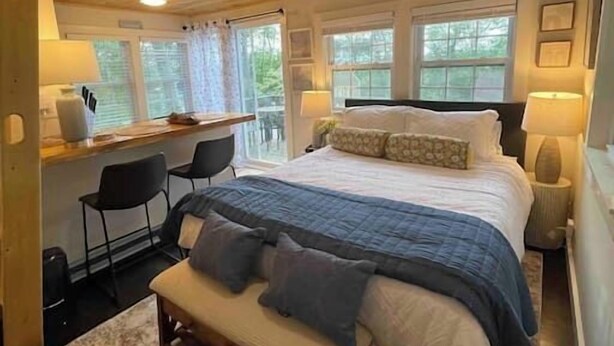 Un dormitorio acogedor con techo de madera, una cama grande con manta azul, un escritorio con silla y una ventana con cortinas.