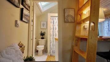 A narrow hallway leading to a bathroom with a skylight, a toilet, and a shower curtain.