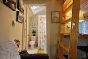 A narrow hallway leading to a bathroom with a skylight, a toilet, and a shower curtain. - Cheerful Cottage with Loft Close to Everything 6 (Edgecomb)