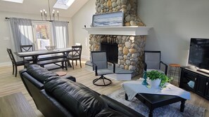 A modern living room with a stone fireplace, a black leather sofa, a dining table with chairs, and a television. - Beautiful newly renovated home with Pool, very close to beaches. (Stafford Township)