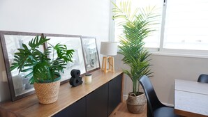 Una habitación con un escritorio de madera, una silla, una planta en maceta, un cuadro enmarco y una lámpara.