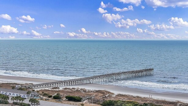 Ein Strand mit einer langen Seebrücke, die sich ins Meer erstreckt, bewölkter Himmel und ruhiger See.