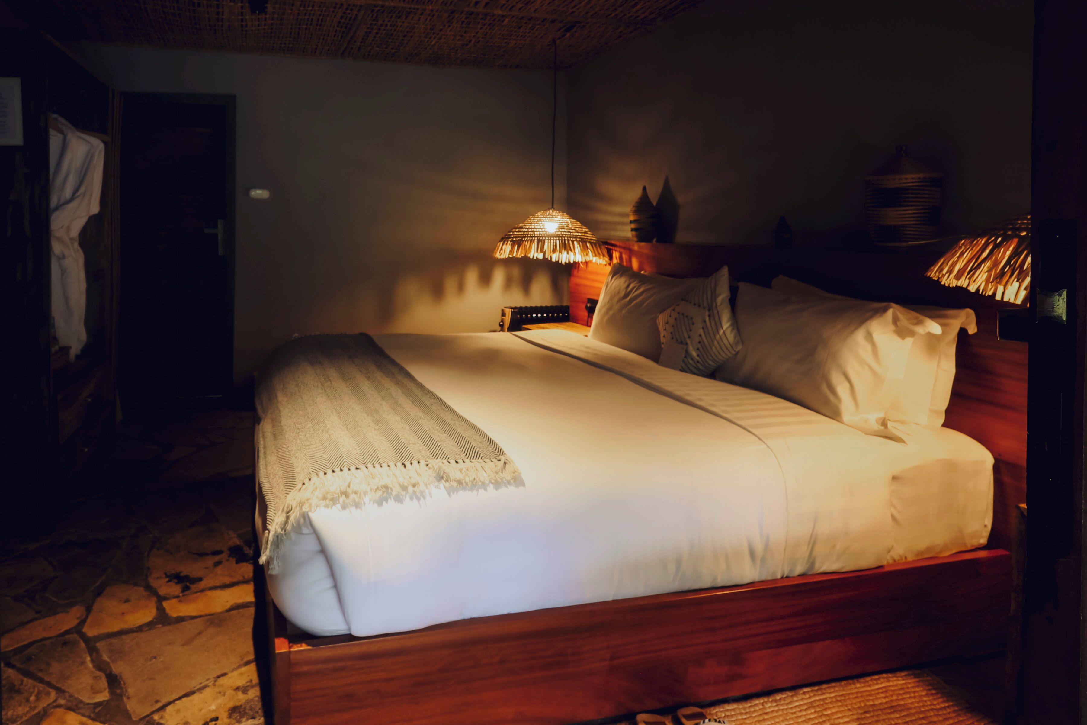 Una cama bien hecha con estructura de madera, una lámpara de noche y una mesita con lámpara.