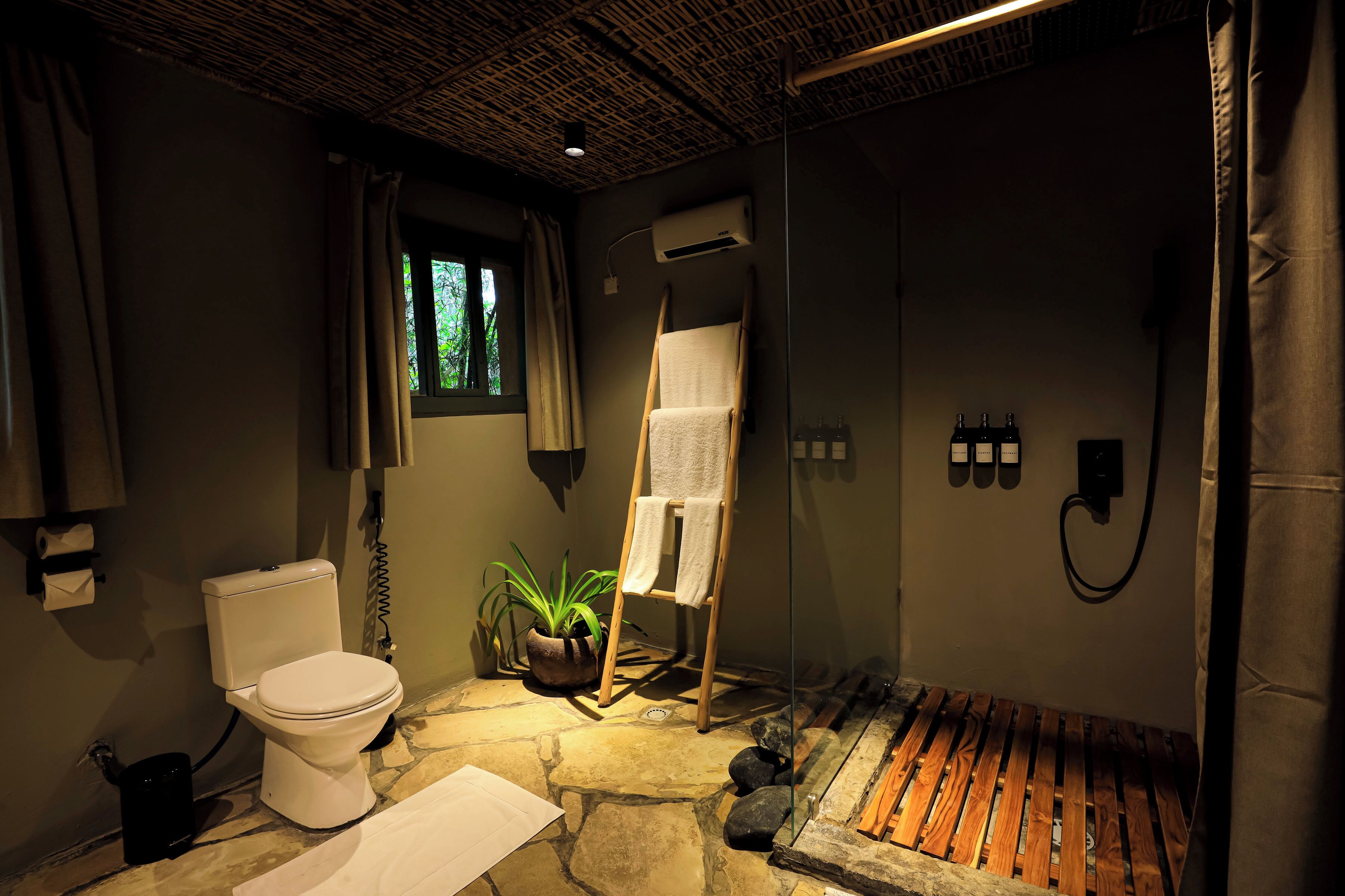 A bathroom with a toilet, a towel rack, a potted plant, and a wooden bench.