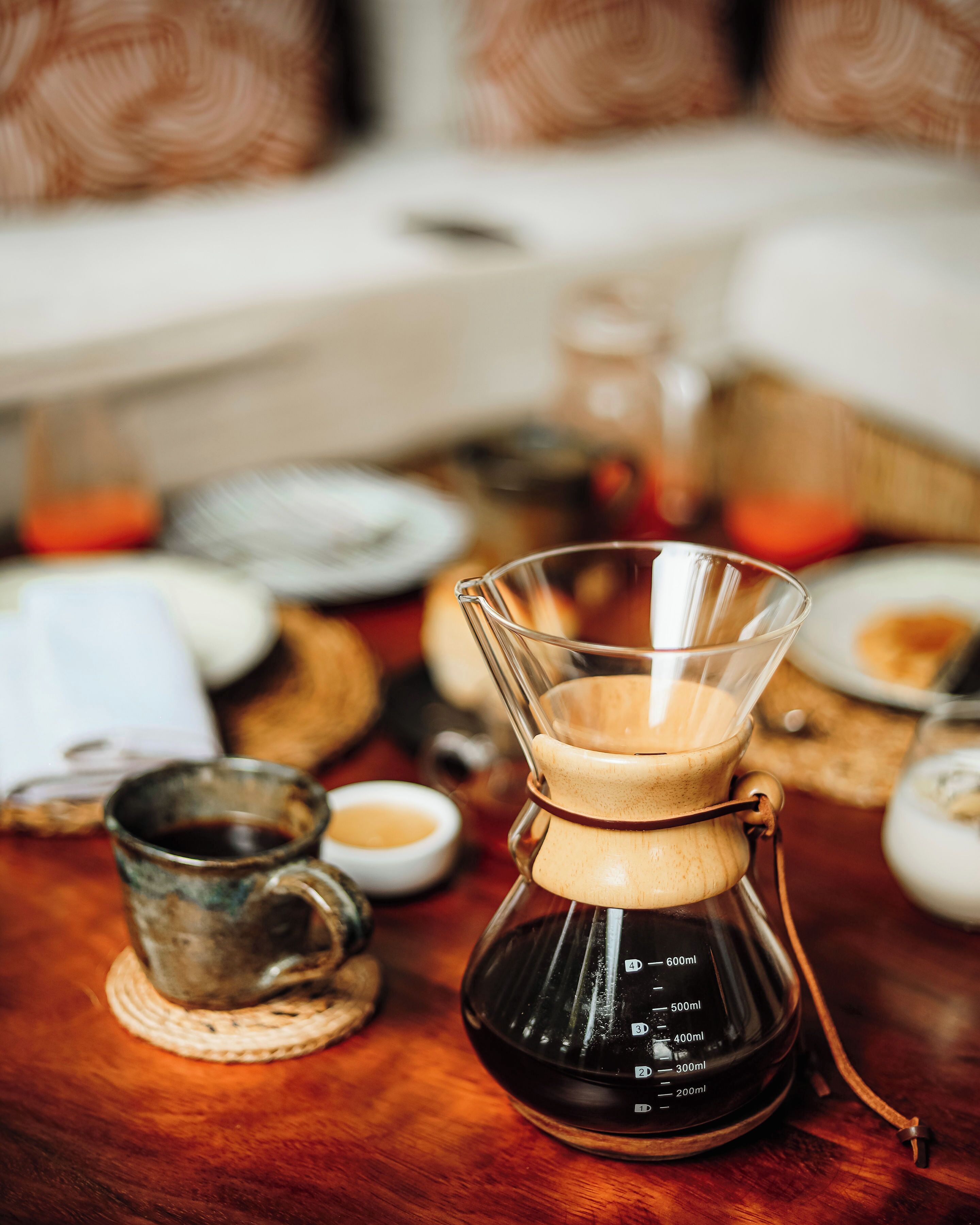 Een koffiezetapparaat op een houten tafel met een kop en schotel, en een glazen kan.