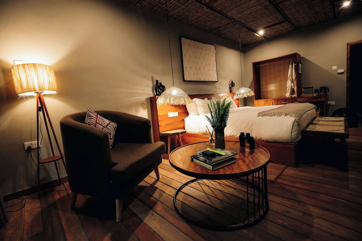 A cozy hotel room with a bed, a chair, a round coffee table, and a lamp.