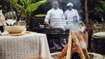 Un área de comedor al aire libre con una parrilla, una mesa con un tazón y un vaso, y un pozo de fuego.