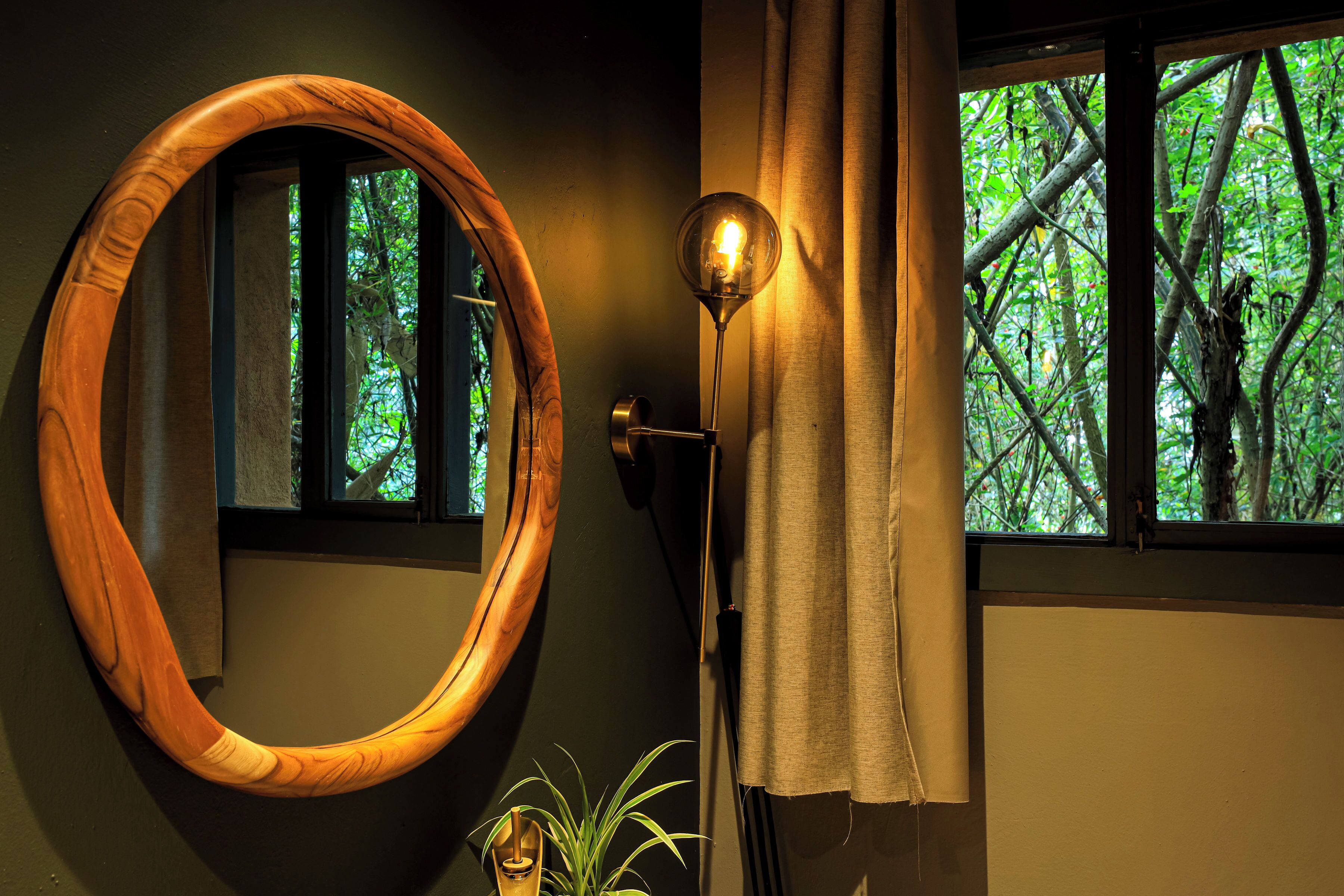 A room with a wooden-framed mirror, a floor lamp, and a window with a view of trees.