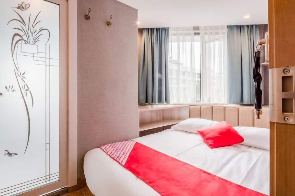 Quarto de hotel com cama, janela com cortinas, mesa de cabeceira e painel decorativo na parede.