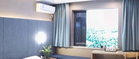 Habitación de hotel con cama, escritorio, silla, ventana con cortinas y una planta en maceta.