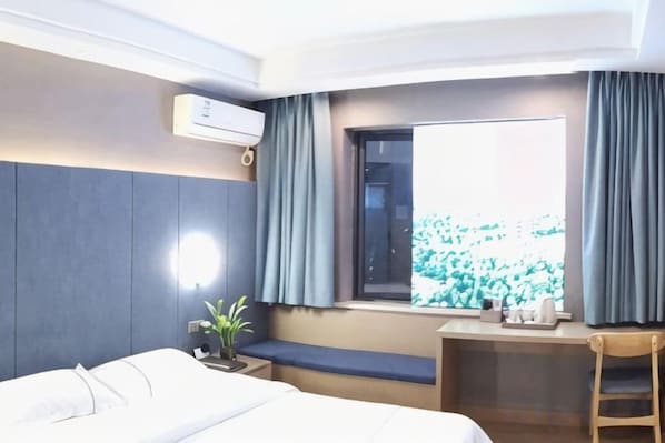 Habitación de hotel con cama, escritorio, silla, ventana con cortinas y una planta en maceta.