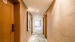 Un couloir d’hôtel avec un tapis à motifs, des portes en bois et des tableaux encadrés accrochés aux murs.
