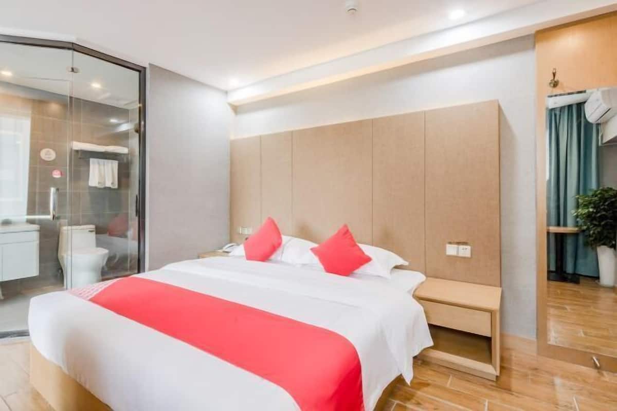 Quarto de hotel moderno com uma cama grande, uma mesa de cabeceira, box de chuveiro em vidro e painel de parede de madeira.