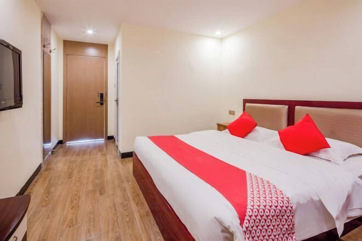 Quarto de hotel com piso de madeira, cama com roupa de cama branca e vermelha, e cabeceira de madeira.