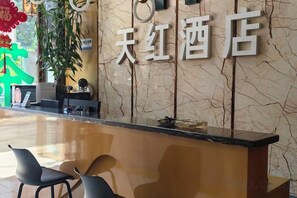 Una recepción de hotel con una pared de mármol y un letrero que dice '天红酒店'. Hay dos sillas frente al mostrador.