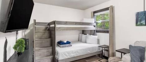 Une chambre avec un lit superposé, une télévision, une petite table et une fenêtre avec des rideaux.
